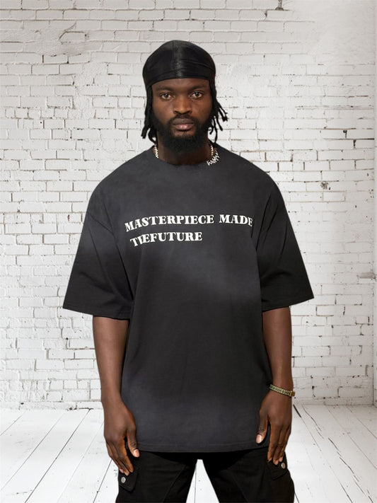 Person wearing a black t-shirt with 'MASTERPIECE MADE TTFUTURE' text against a white brick wall.